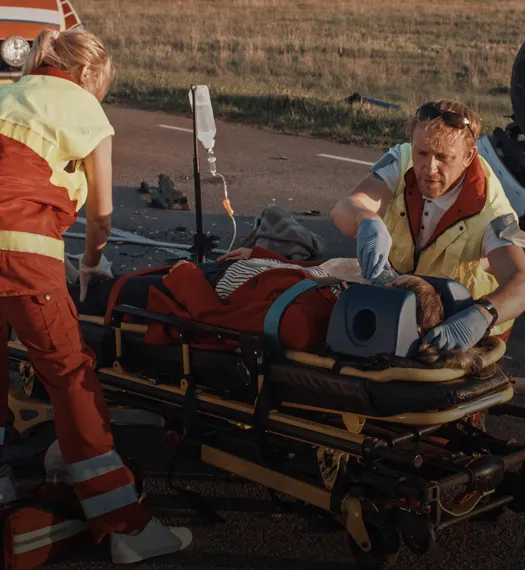 Two paramedics attending to an injured person on a stretcher with a cervical collar and IV drip.