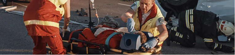 Emergency responders attend to an injured person on a stretcher near an overturned vehicle.