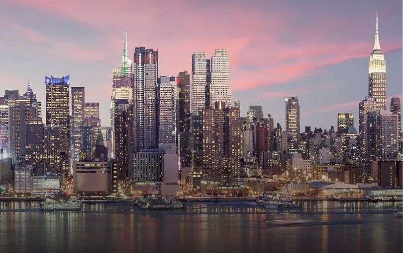 Panoramic view of a city skyline at dusk with illuminated skyscrapers and a pink sky.