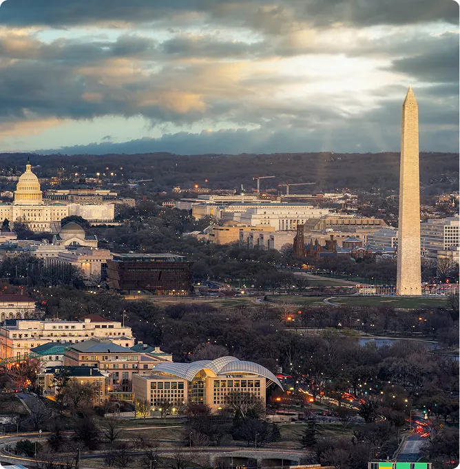 Aerial view of Washington, D.C. featuring the Washington Monument and U.S. Capitol under a cloudy sky.