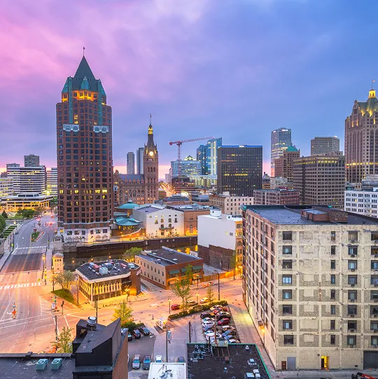 Downtown cityscape at dusk with illuminated buildings under a purple and blue sky.