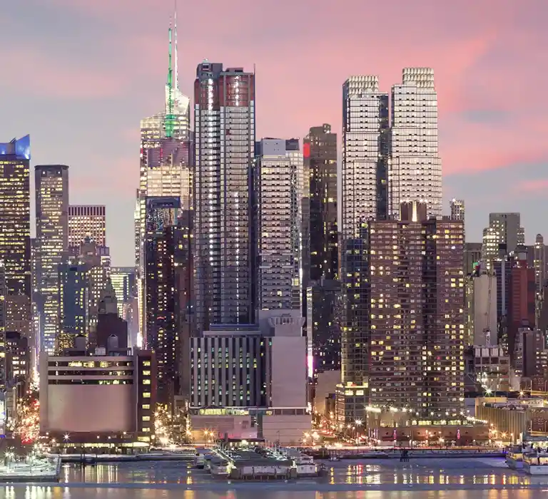 City skyline at dusk with illuminated skyscrapers and a pinkish sky background.