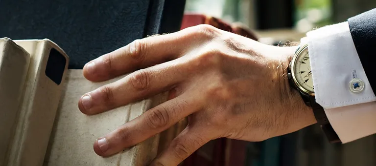 Close-up of a male hand wearing a watch, reaching for a book on a shelf.