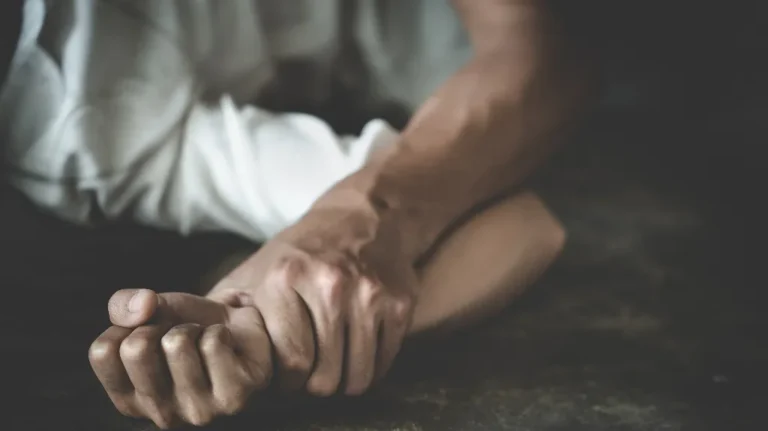 Two hands clasped tightly on a dark surface, one arm covered by a white garment.