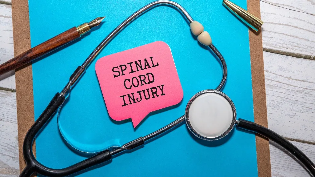 Stethoscope, fountain pen, and pink speech bubble with "SPINAL CORD INJURY" text on blue clipboard.