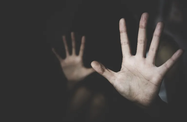 Two outstretched hands in dim lighting against a dark background, palms facing forward.