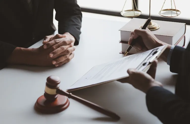 Two professionals in formal attire at a desk with legal books, a gavel, and scales of justice.