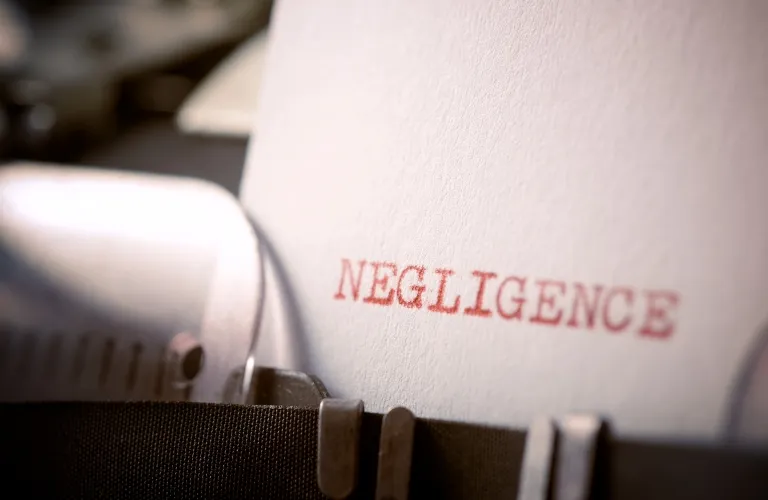 Close-up of a typewriter with the word "NEGLIGENCE" typed in red ink on white paper.