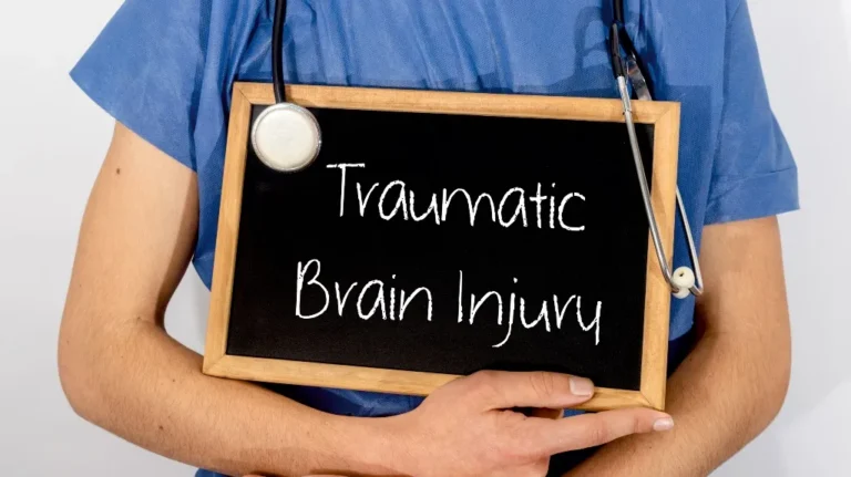 Healthcare professional in blue scrubs holding a chalkboard with "Traumatic Brain Injury" text and a stethoscope.
