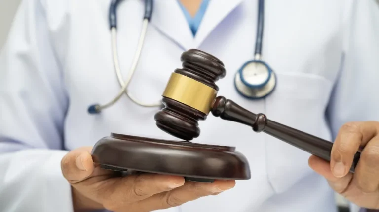 Close-up of a person in a white medical coat holding a judge's gavel and sound block.