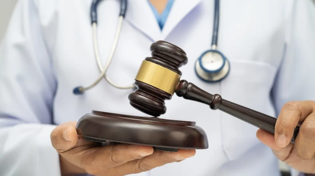 Close-up of a person in a white medical coat holding a judge's gavel and sound block.