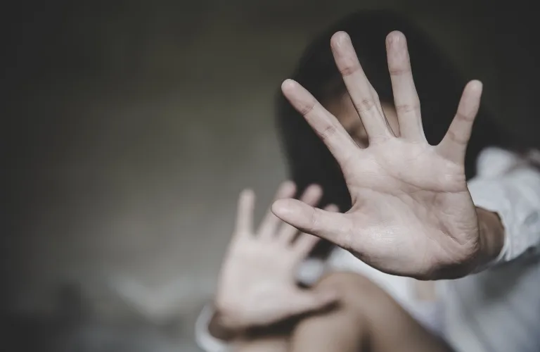 Person with outstretched hands raised in a defensive gesture against a dark background.